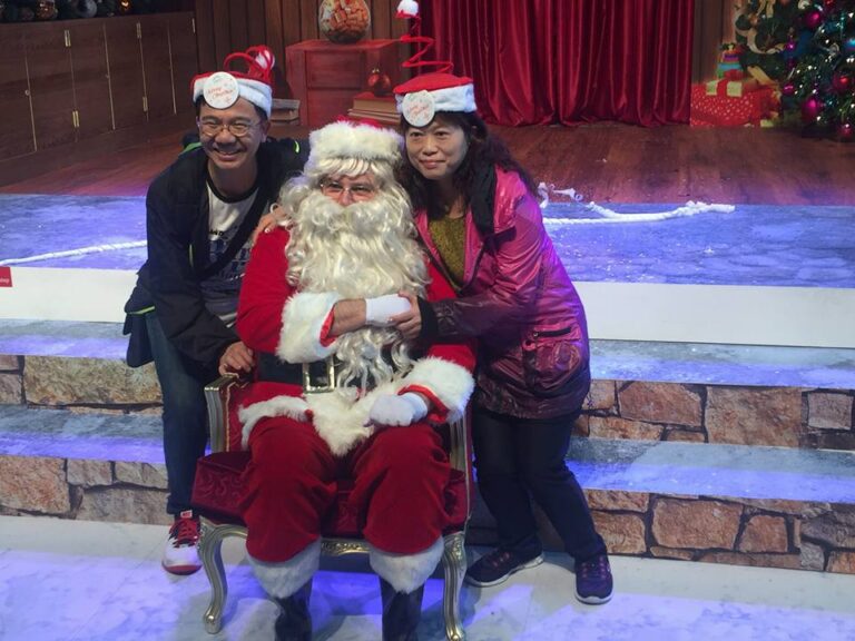 HK performer dress as Santa, taking picture with two tourists who wearing Xmas hat in front of the Xmas backdrop at a Hong Kong Christmas function.