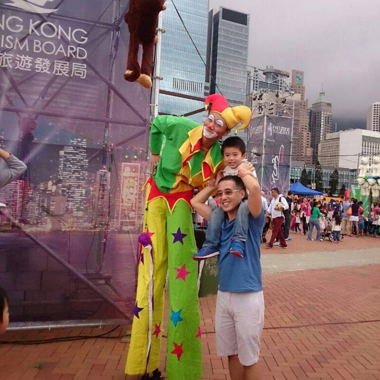 Stiltwalk wearing jester costume taking photo with dad with child on shoulders