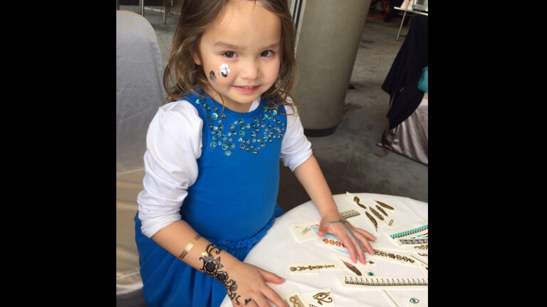 A little child having temporary henna tattoos on her both hands and face at a kids birthday party