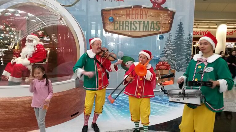 Xmas band trio playing with santa sitting in giant snow globe in background.