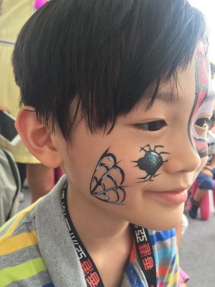 HK face painter draw a spider face paint on a kid face at a corporate Halloween event