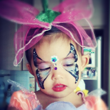A professional face painter in HK draw her signature butterfly face paint on a little girl face at a corporate family fun day event