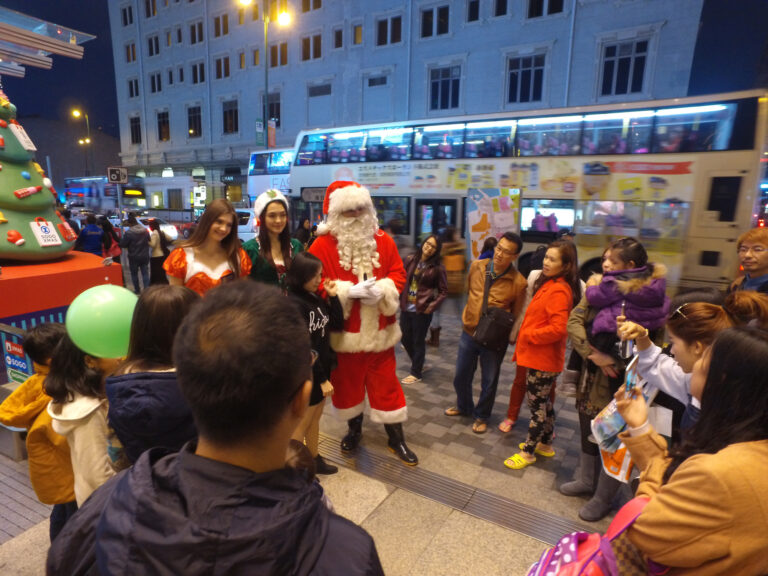 HK models and performer dress as Santa ,Santa girl and Elf standing outside Hong Kong greeting and photo taking with the guests at a Christmas corporate event.
