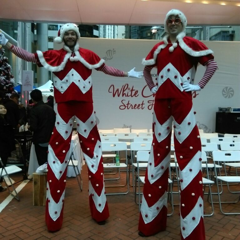 Two candy cane looking stilt walkers standing next to Swire stage