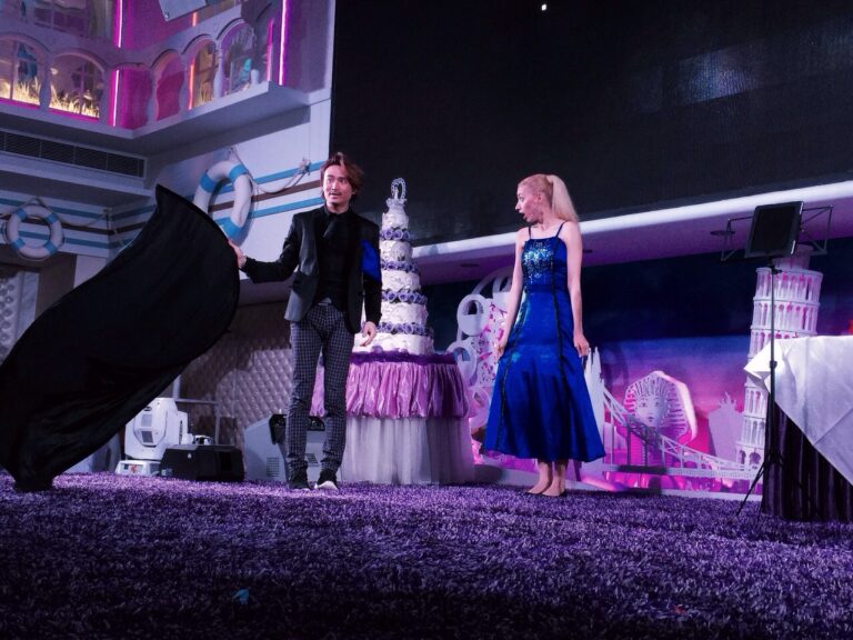 Magician in Hong Kong standing in front of a wedding cake ,holding a black cloth ,performing stage magic with is assistant who wearing a blue dress at a corporate event