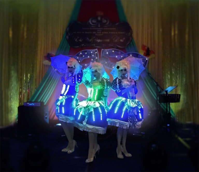 Three dancers in period costume with LED lights and umbrellas