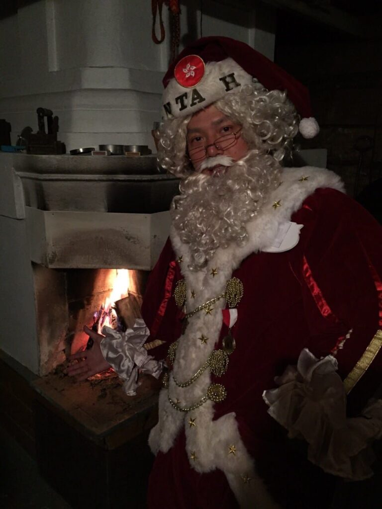 Chinese Santa Mario by the fire place staying warm in maroon colored santa suit