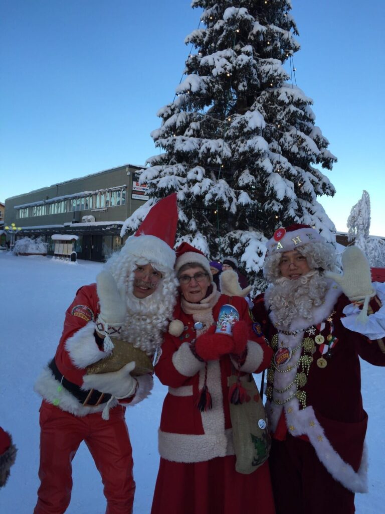 Standing in front of christmas tree with other santa, chinese santa mario is happy and his friend is also happy with finnish local women in tow