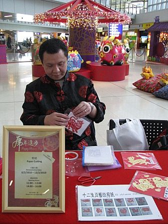 Artist in HK putting a dog zodiac paper cut out to the guest at the HKIA