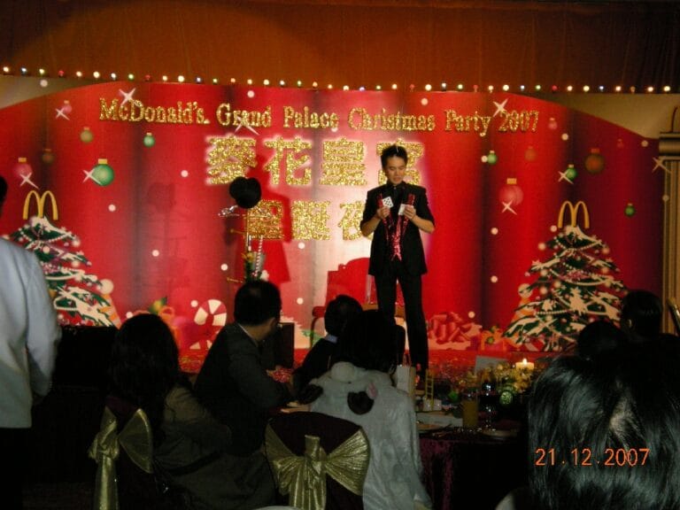 Magician standing next to the magic hat and Christmas tree performing stage card magic at Hong Kong McDonald corporate event.