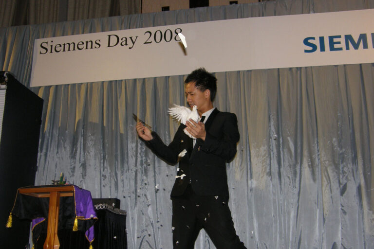 Magician in Hong Kong standing nest to the magic table , performing stage dove magic at a corporate event