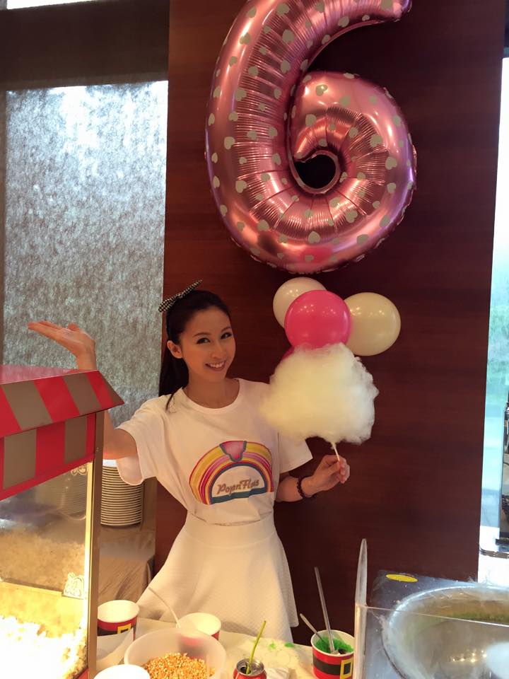 Model serving candy floss with popcorn machine in foreground