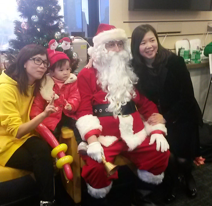 Santa with two ladies and a baby sitting in front of a Christmas tree at a Kong Kong corporate event.