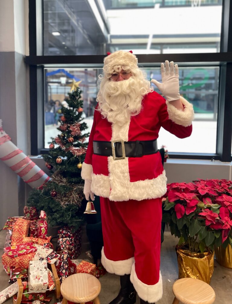 Santa in red suit in front of a christmas tree