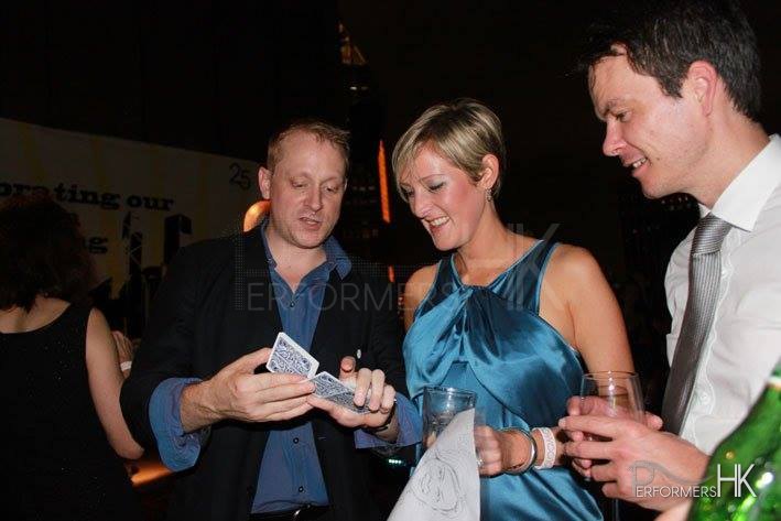 Magician playing with cards to two guests holding drinks