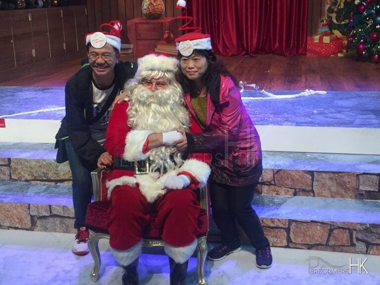 HK performer dress as Santa, taking picture with two tourists who wearing Xmas hat in front of the Xmas backdrop at a Hong Kong Christmas function.