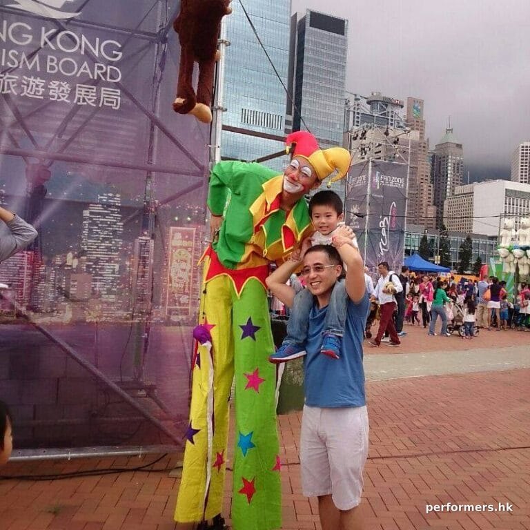 Stiltwalk wearing jester costume taking photo with dad with child on shoulders