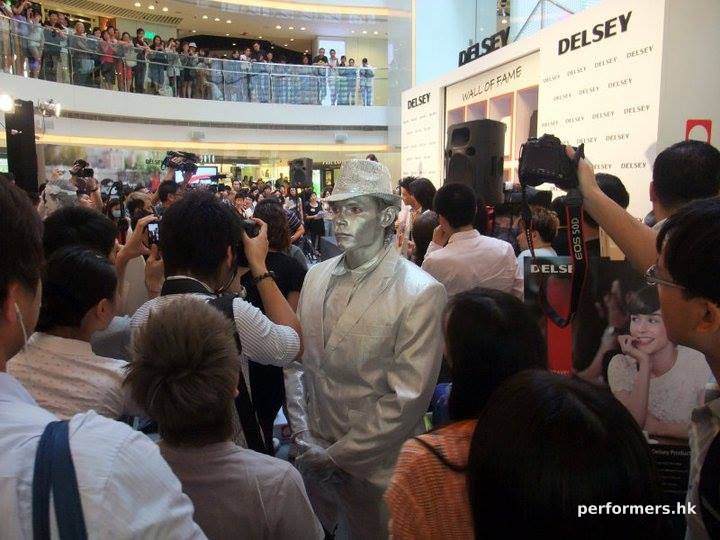 Silver man human statue standing in a crowd with lots of photographs being taken