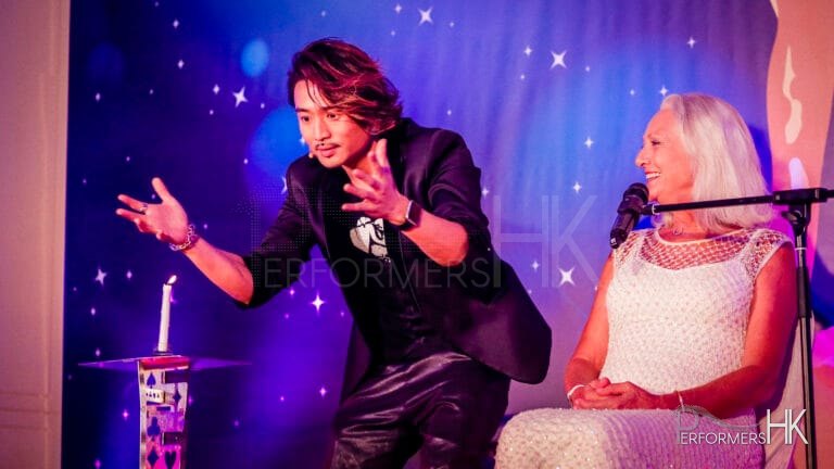 Magician standing next to the table with a lighted candle on it , performing stage magic to the chairwoman at Hong Kong Dog Rescue annual dinner in Aberdeen Marina Club
