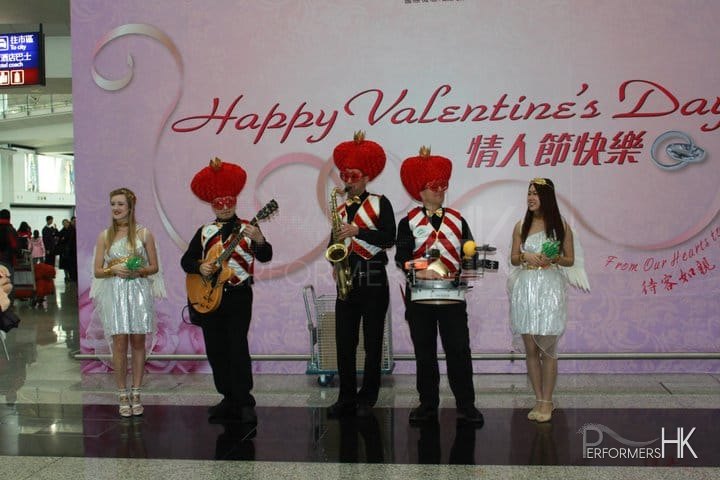 Roving three piece band with drum sax and guitar walking around Hong Kong airport wearing valentine day costumes