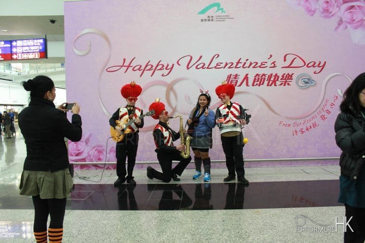 Three roving musicians dressed in red and white vests and love heart hats serenading a girl