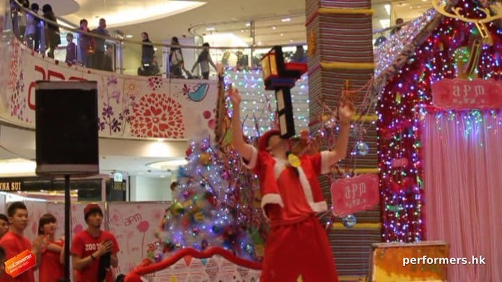 HK juggler performing at a corporate shopping mall event ,  holding six cigar boxes with his chin and the audience are impresses by him