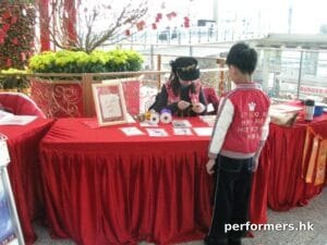 A female artist working on a Chinese knotting gift for child on a red table with the background of a flower pot at the Hong Kong Airport