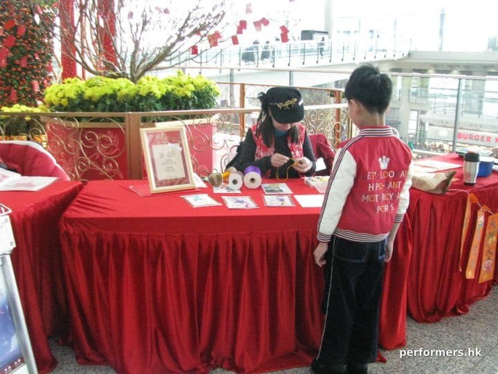 A female artist working on a Chinese knotting gift for child on a red table with the background of a flower pot at the Hong Kong Airport
