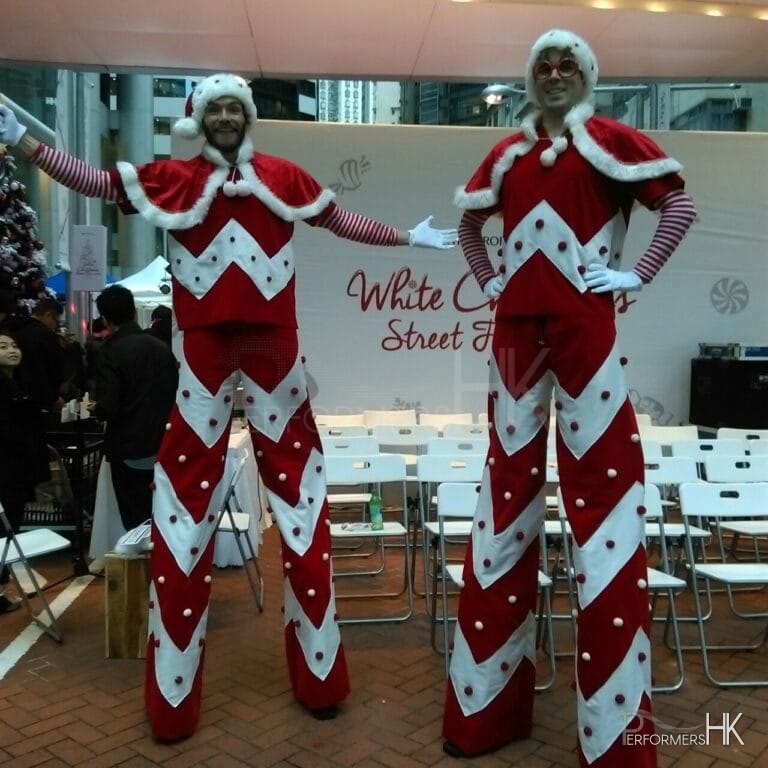 Two candy cane looking stilt walkers standing next to Swire stage