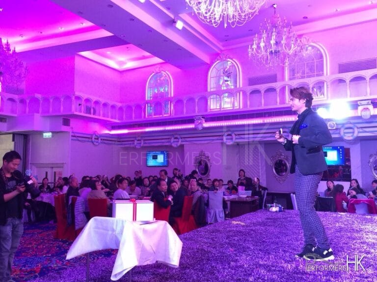 HK magician standing on a purple stage performing his stage act with the mobile borrow from the audience at a corporate annual dinner