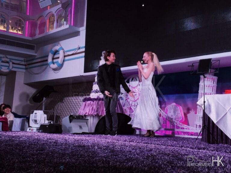 Magician in Hong Kong standing on the stage ,performing stage magic with is assistant and change her dress from blue to white at a corporate event