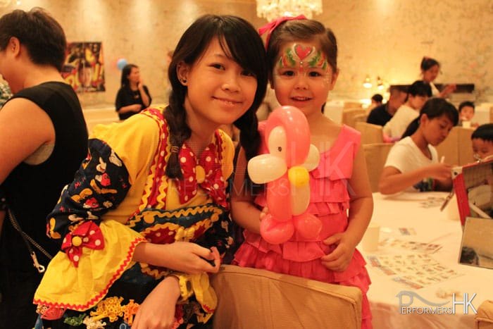 Hong Kong walk around balloon twister dress as a clown with a Mickey Mouse clown costume taking picture with a little girl wearing pink ,holding a pink Pingu at a Children birthday party