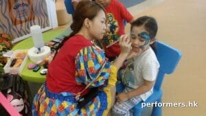 Face painter in HK very focused, drawing a dolphin face paint on a child at a school event
