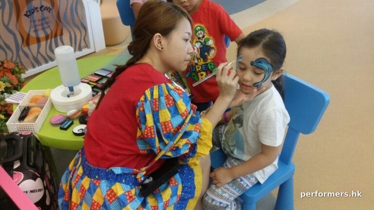 Face painter in HK very focused, drawing a dolphin face paint on a child at a school event