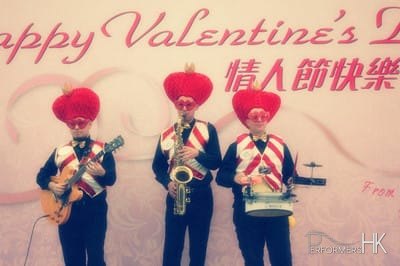 Three musicians wearing valentine day costumes with large love heart hat and red and white vests