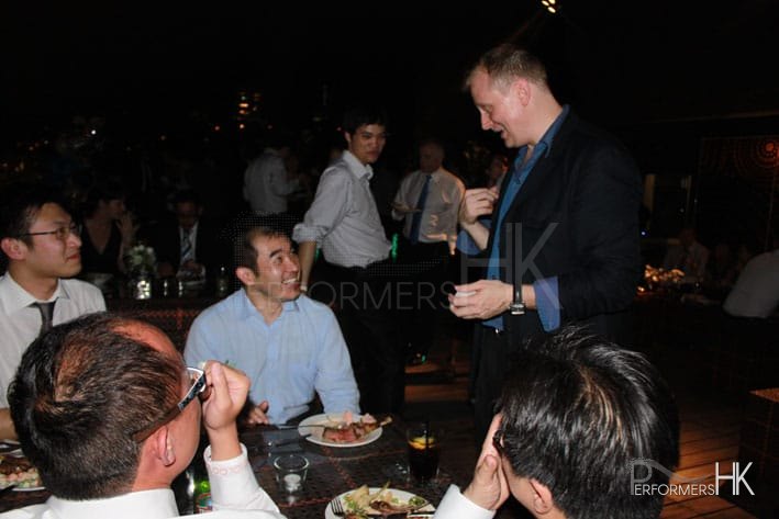 Walk around Magician in HK performing table card magic to four gentlemen at a roof top corporate event in Wan Chai