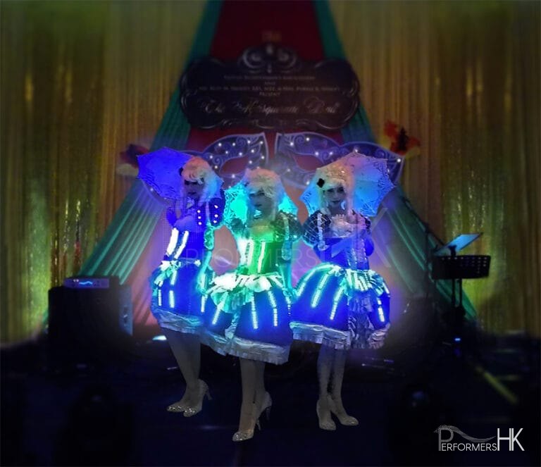 Three dancers in period costume with LED lights and umbrellas