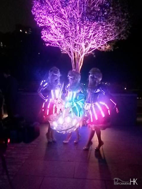 The LED dancers donning period dresses standing under lit up tree