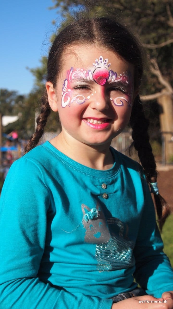 A Hong Kong face painter draw a pink princess face paint for a girl in blue shirt at a corporate school event.