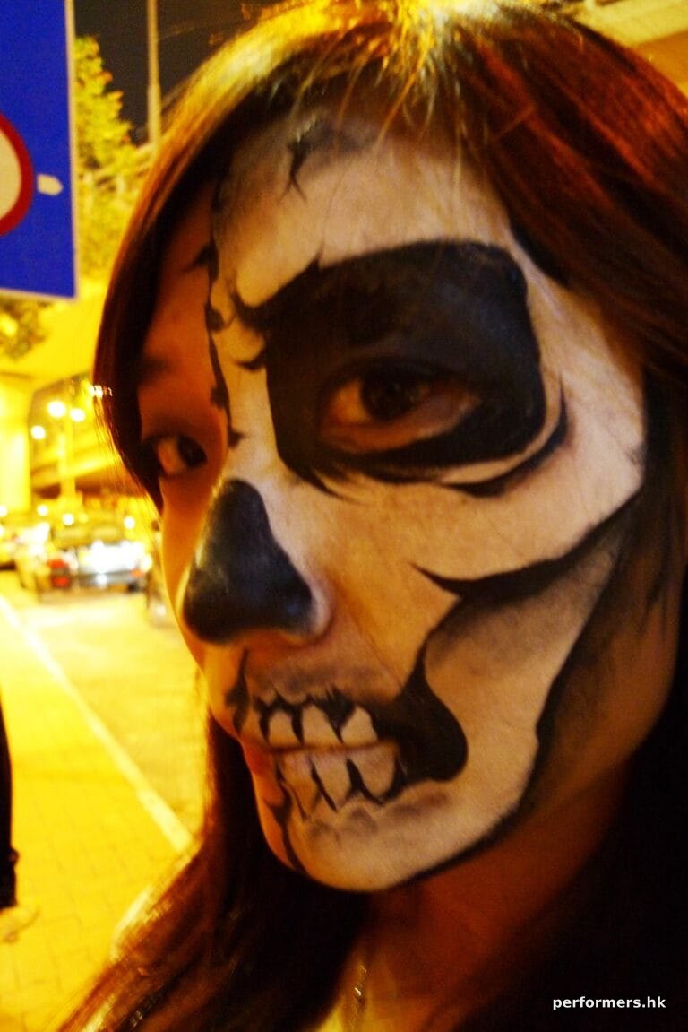 A female face painter draw a black and white skull face paint to join a Halloween event in HK