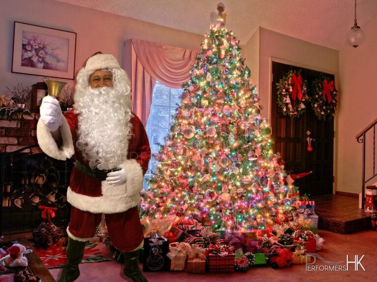 Santa performer in HK wearing Santa costume,standing in front of a Xmas tree and holding up a bell,taking picture reference for a Christmas corporate event .