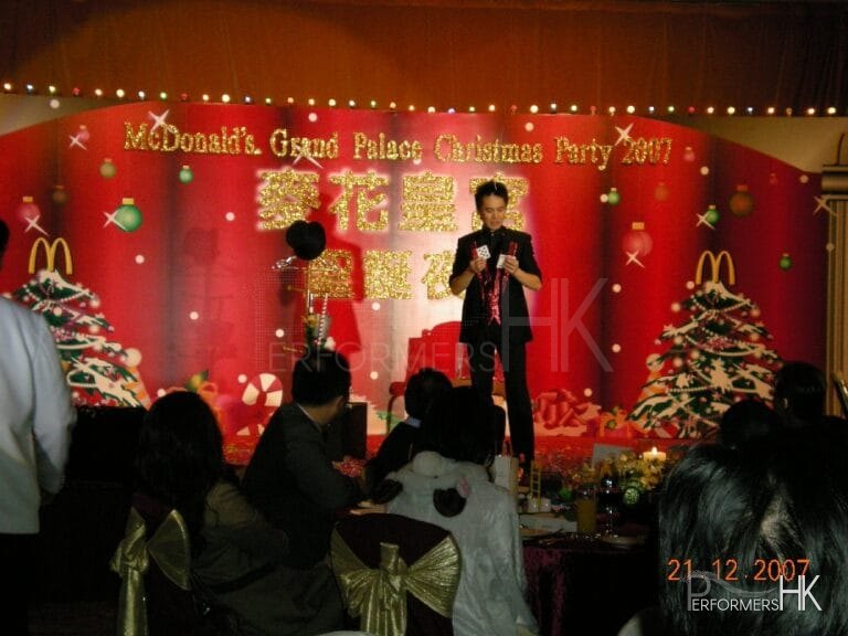 Magician standing next to the magic hat and Christmas tree performing stage card magic at Hong Kong McDonald corporate event.