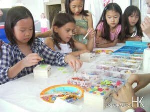 Five girls is choosing different materials  to decorate their own jewelry box at a corporate kids event