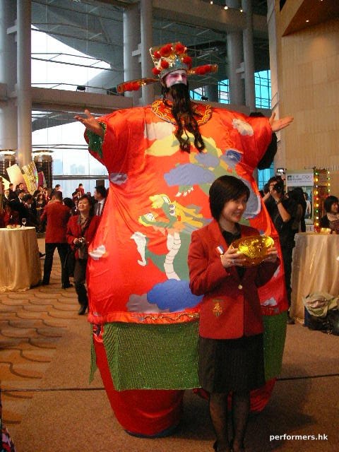 Stiltwalker in HK wearing inflatable costume taking picture with a lady holding a yuan bao at a Chinese New Year Annual dinner