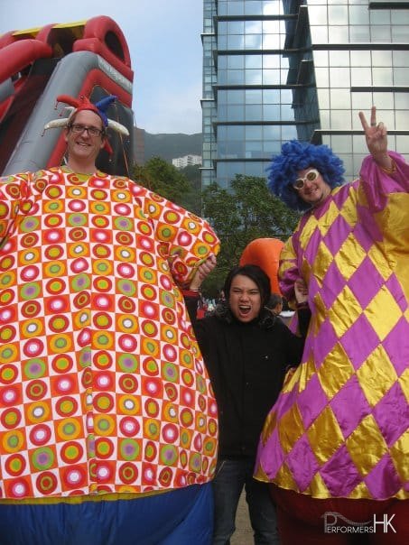 Two Hong Kong stilt-walkers squeezing a man between them at the Cycberport