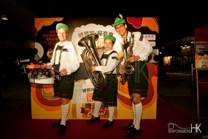Three walk around musicians drum sax and tuba donning German attire and posing