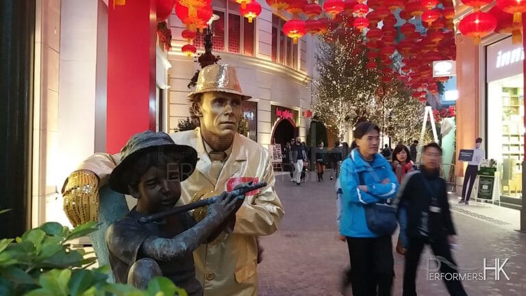 Golden statue standing next to bronze statue of boy playing the flute