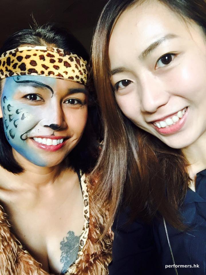 A face painter in HK taking picture with her at a juggle themed corporate event after she painted a blue and white leopard half face paint for her.
