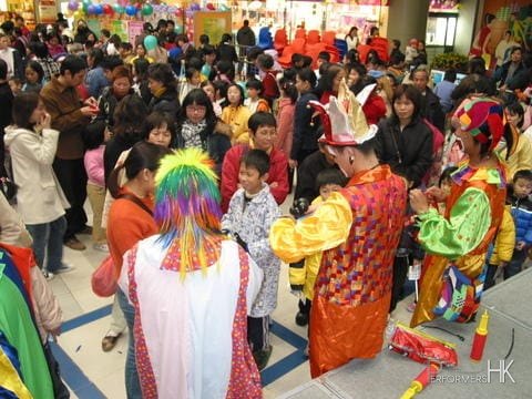 Three walk around clown twisting balloons for the children at a school fair