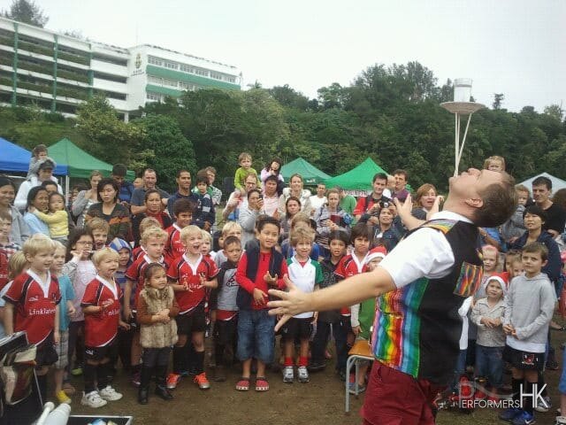 Performer balancing a glass of water on three chopstick whilst a large crowd watches